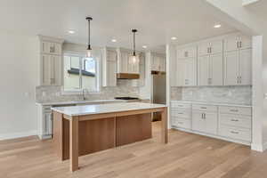 Kitchen featuring a center island, hanging light fixtures, built in fridge, light hardwood / wood-style floors, and decorative backsplash