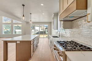 Kitchen with custom exhaust hood, high end stove, sink, decorative light fixtures, and a kitchen island