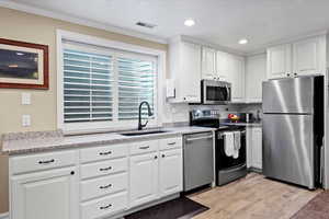 Kitchen featuring white cabinets, light wood-type flooring, crown molding, sink, and appliances with stainless steel finishes