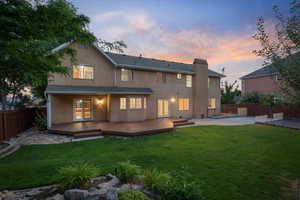 Back house at dusk featuring a wooden deck, french doors, and a lawn