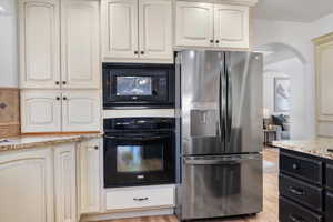 Kitchen featuring light wood-type flooring, light stone counters, and black appliances