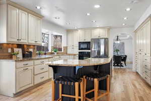 Kitchen featuring a kitchen bar, a center island, light stone countertops, cream cabinets, and black appliances