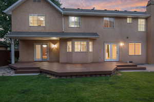 Back house at dusk featuring a lawn, a deck, and french doors