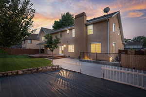 Back house at dusk with a wooden deck and a yard