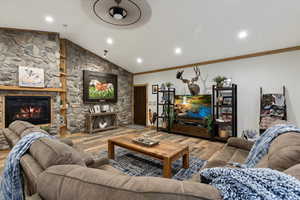 Living room with a stone fireplace, crown molding, hardwood / wood-style flooring, and lofted ceiling