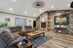 Living room with vaulted ceiling, a fireplace, crown molding, and hardwood / wood-style floors