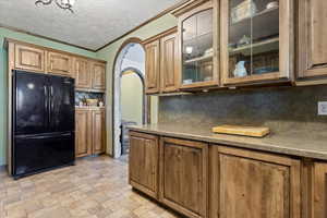 Kitchen featuring backsplash, black refrigerator, crown molding, a textured ceiling, and light tile patterned flooring