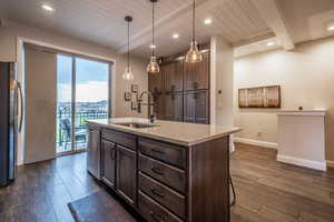 Kitchen featuring stainless steel appliances, beamed ceiling, sink, light stone countertops, and dark hardwood / wood-style floors