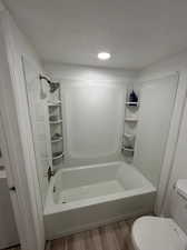 Bathroom with a textured ceiling, hardwood / wood-style flooring, shower / bathing tub combination, and toilet