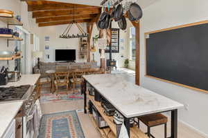 Kitchen featuring light hardwood / wood-style floors, gas range, a wood stove, and vaulted ceiling with beams