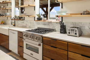 Kitchen featuring range, dishwashing machine, tasteful backsplash, light stone counters, and sink
