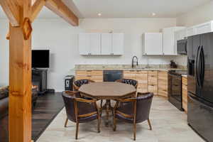 Kitchen with light hardwood / wood-style flooring, black appliances, white cabinets, sink, and light stone countertops