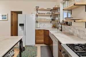 Kitchen with cooktop, light stone counters, light hardwood / wood-style floors, decorative backsplash, and white refrigerator with ice dispenser