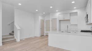 Kitchen with white cabinetry, sink, light hardwood / wood-style flooring, and range