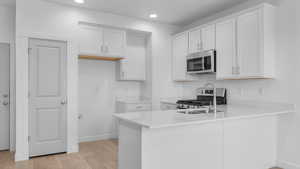 Kitchen with white cabinetry, kitchen peninsula, stainless steel appliances, and light hardwood / wood-style floors