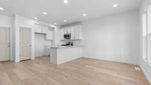 Kitchen featuring appliances with stainless steel finishes, white cabinets, kitchen peninsula, and light wood-type flooring