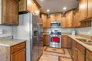 Kitchen with stainless steel appliances, light stone counters, sink, and light hardwood / wood-style flooring