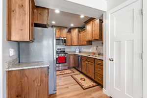 Kitchen featuring light hardwood / wood-style flooring, a textured ceiling, light stone counters, sink, and appliances with stainless steel finishes