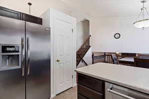 Kitchen featuring stainless steel fridge, dark brown cabinetry, hanging light fixtures, and light tile patterned floors