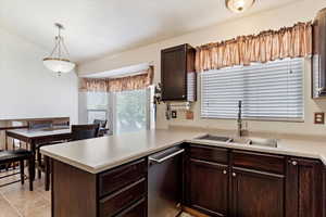 Kitchen with decorative light fixtures, kitchen peninsula, sink, dishwasher, and light tile patterned floors