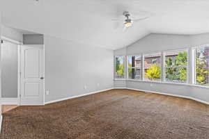 Carpeted empty room featuring plenty of natural light, ceiling fan, and lofted ceiling