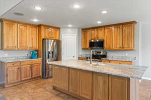 Kitchen with stainless steel appliances, light stone countertops, a kitchen island with sink, and light tile patterned floors