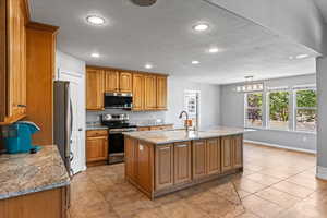 Kitchen featuring light tile patterned floors, light stone counters, a kitchen island with sink, stainless steel appliances, and sink