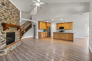 Unfurnished living room with a stone fireplace, a high ceiling, light wood-type flooring, and ceiling fan