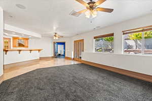 Unfurnished living room featuring light carpet, ceiling fan, and a textured ceiling