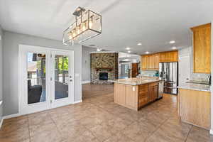 Kitchen featuring appliances with stainless steel finishes, sink, a kitchen island with sink, light stone countertops, and a large fireplace