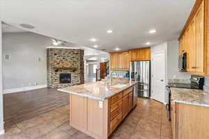 Kitchen featuring black appliances, a fireplace, light wood-type flooring, sink, and a kitchen island with sink