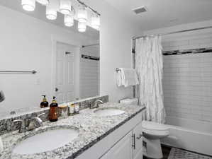 Full bathroom with double vanity, shower / bath combo, and toilet