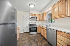 Kitchen featuring dark tile patterned flooring, light brown cabinets, appliances with stainless steel finishes, and sink