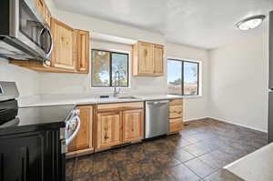 Kitchen with plenty of natural light, sink, appliances with stainless steel finishes, and dark tile patterned floors