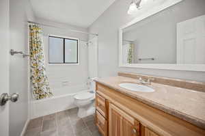 Full bathroom with tile patterned flooring, shower / bath combo with shower curtain, toilet, and vanity