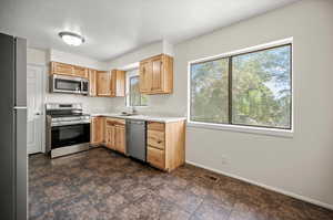 Kitchen with stainless steel appliances, light brown cabinets, sink, a textured ceiling, and dark tile patterned flooring