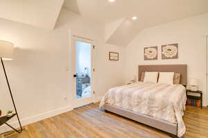 Bedroom with light hardwood / wood-style floors, vaulted ceiling, and access to exterior