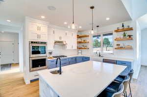 Kitchen with pendant lighting, blue cabinetry, light hardwood / wood-style floors, backsplash, and a kitchen island with sink