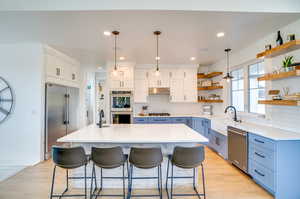 Kitchen featuring blue cabinets, hanging light fixtures, white cabinets, appliances with stainless steel finishes, and backsplash