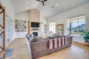 Living room featuring built in features, high vaulted ceiling, a fireplace, and light hardwood / wood-style floors