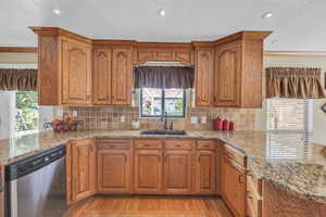 Kitchen featuring dishwasher, light hardwood / wood-style floors, light stone countertops, decorative backsplash, and sink