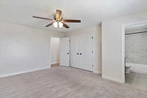 Unfurnished bedroom featuring ensuite bathroom, light carpet, ceiling fan, and a closet