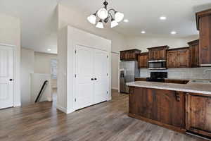 Kitchen with dark brown cabinets, backsplash, hardwood / wood-style floors, appliances with stainless steel finishes, and sink