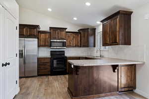 Kitchen with stainless steel appliances, vaulted ceiling, sink, backsplash, and light wood-type flooring