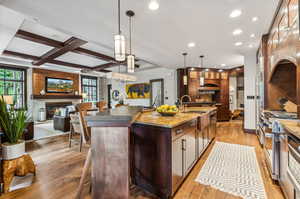 Kitchen featuring decorative light fixtures, light wood-type flooring, an island with sink, beam ceiling, and coffered ceiling