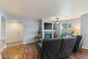 Living room featuring ceiling fan, a fireplace, and dark wood-type flooring