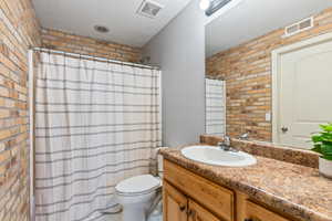 Bathroom with brick wall, toilet, and vanity