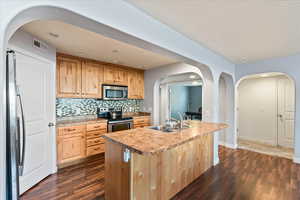 Kitchen with tasteful backsplash, stainless steel appliances, a center island with sink, sink, and dark hardwood / wood-style floors