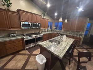 Kitchen featuring appliances with stainless steel finishes, vaulted ceiling, sink, pendant lighting, and a kitchen island with sink