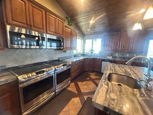 Kitchen featuring appliances with stainless steel finishes, tasteful backsplash, vaulted ceiling, and light stone countertops